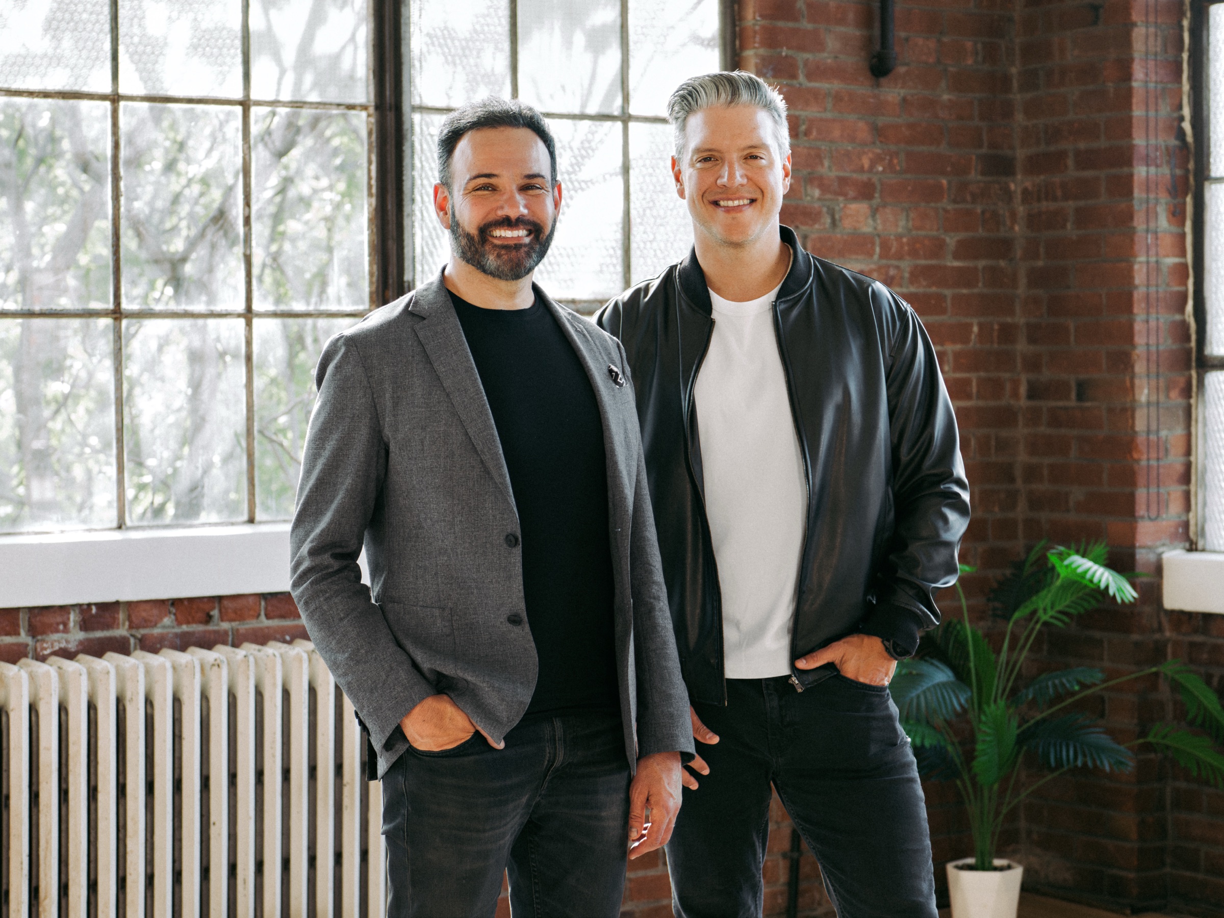 SELLIT9 founders Josh and Oswaldo standing together in a sunlit industrial loft.